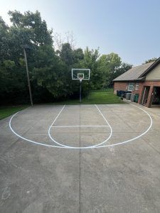 A basketball court in a driveway in front of a house.