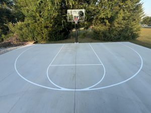 A concrete basketball court with a basketball hoop and trees in the background.
