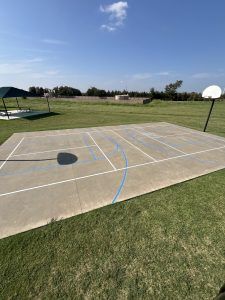 There is a basketball court in the middle of a grassy field.