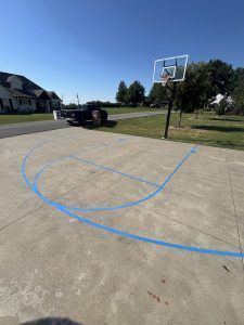 A basketball court in a driveway with a truck parked in the background.