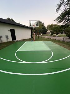 A green and white basketball court in front of a house.