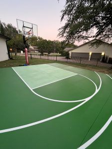A basketball court in a backyard with a basketball hoop.