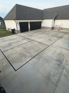 A large concrete driveway in front of a house with two garage doors.