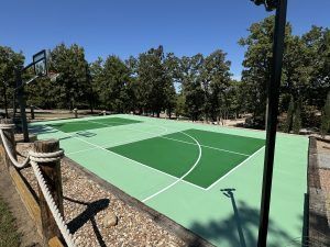 A basketball court is surrounded by trees and a rope fence.