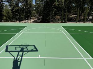 A green basketball court with a shadow of a basketball hoop on it.