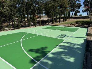 A green basketball court with trees in the background.
