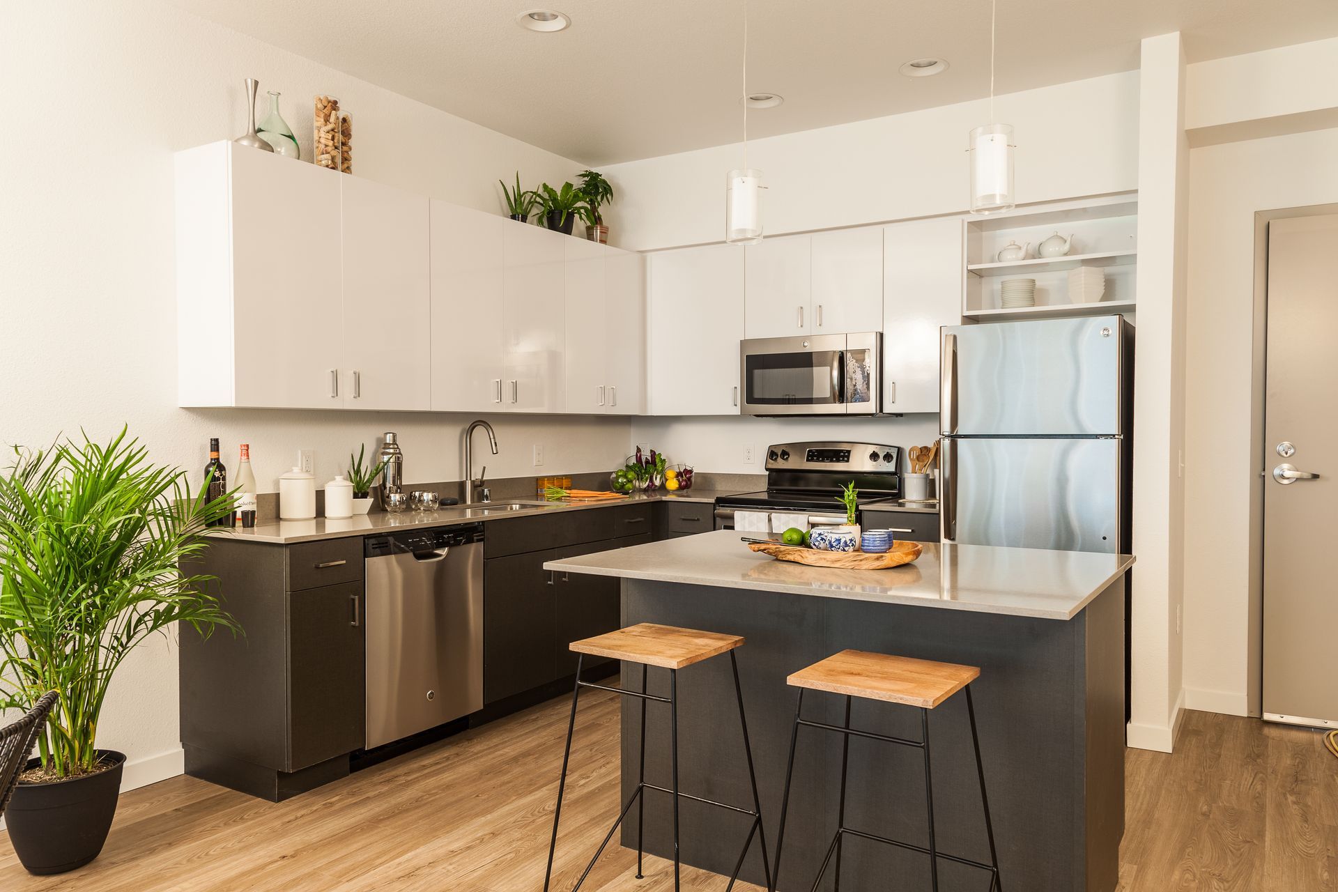 Cuisine moderne avec armoires grises et blanches, électroménagers en acier inoxydable et un îlot avec tabourets.