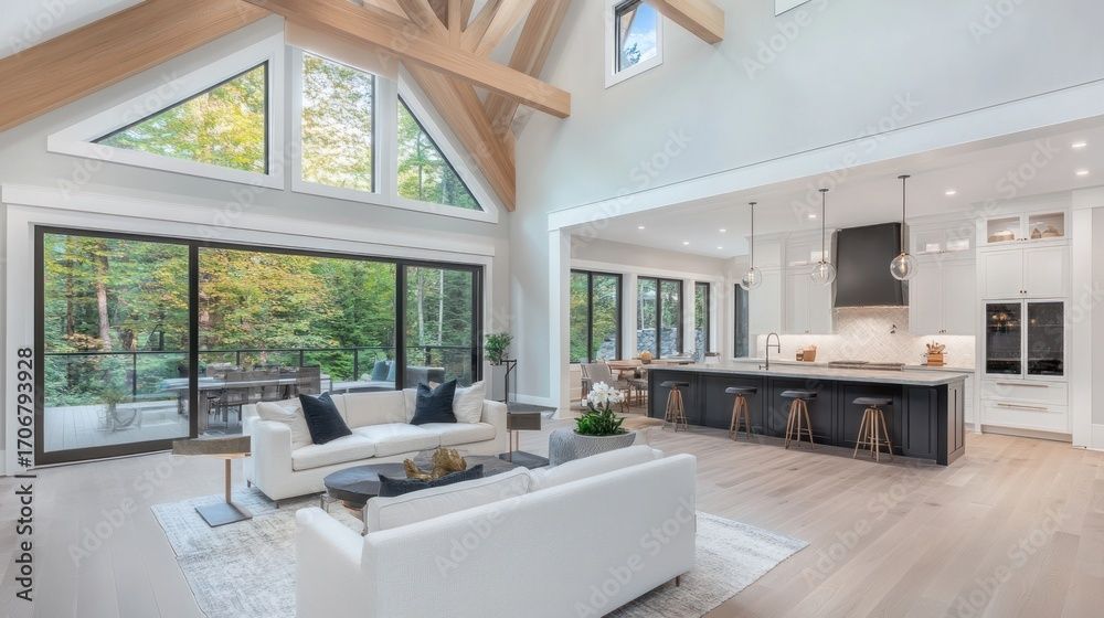 Salon spacieux et moderne avec de grandes fenêtres, cuisine ouverte, canapés blancs et poutres apparentes.