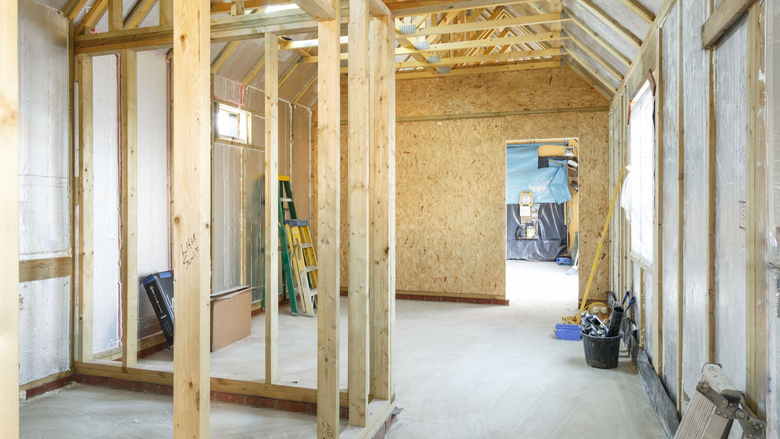 Intérieur d'un bâtiment en construction, avec charpente en bois visible, murs non finis et sol en béton.