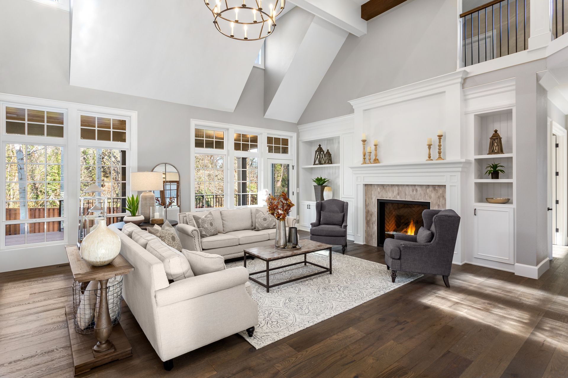 Spacious living room with high ceilings, fireplace, light-colored couches, and large windows.
