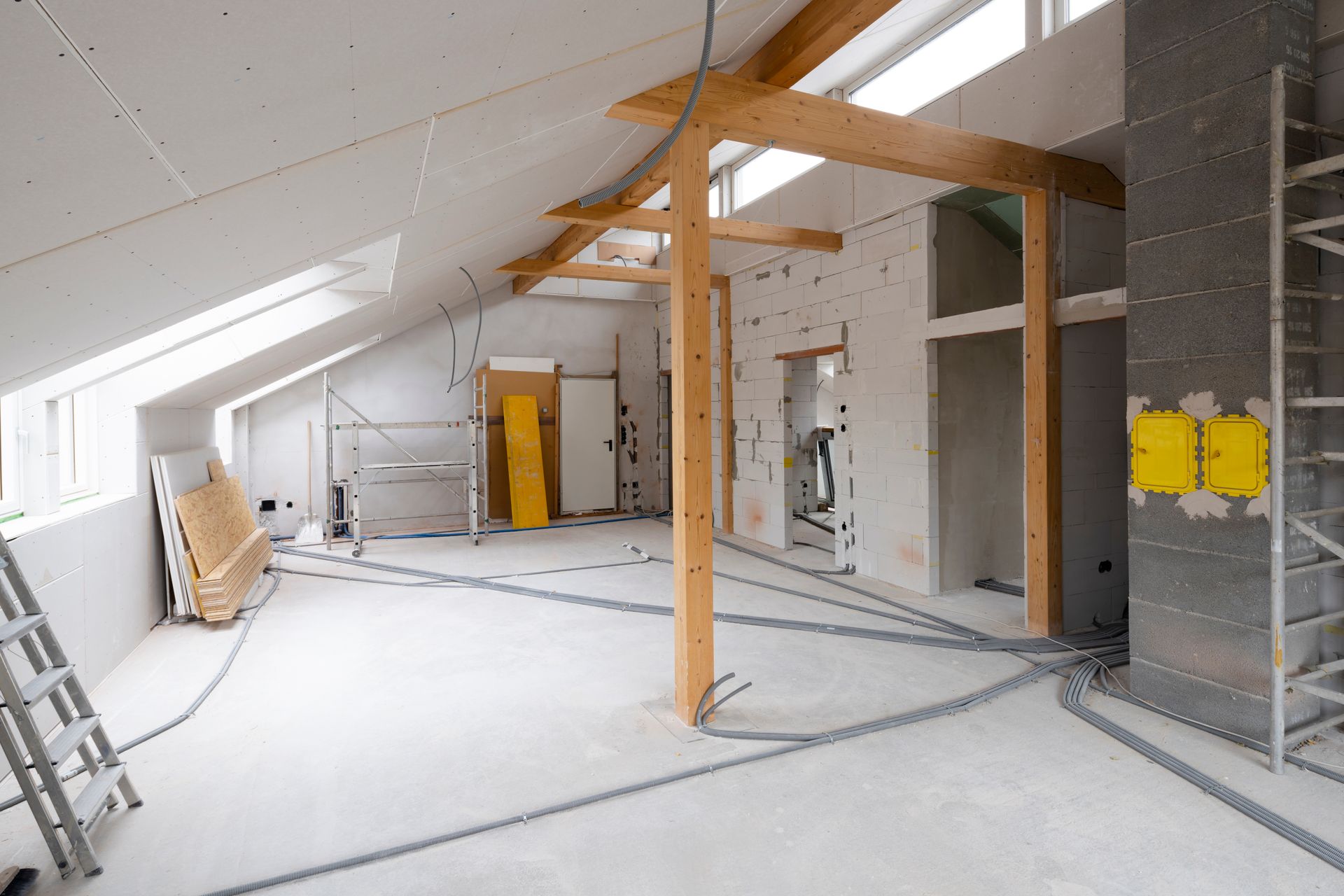 Intérieur d'une pièce en construction avec poutres apparentes, cloisons sèches et câblage électrique.