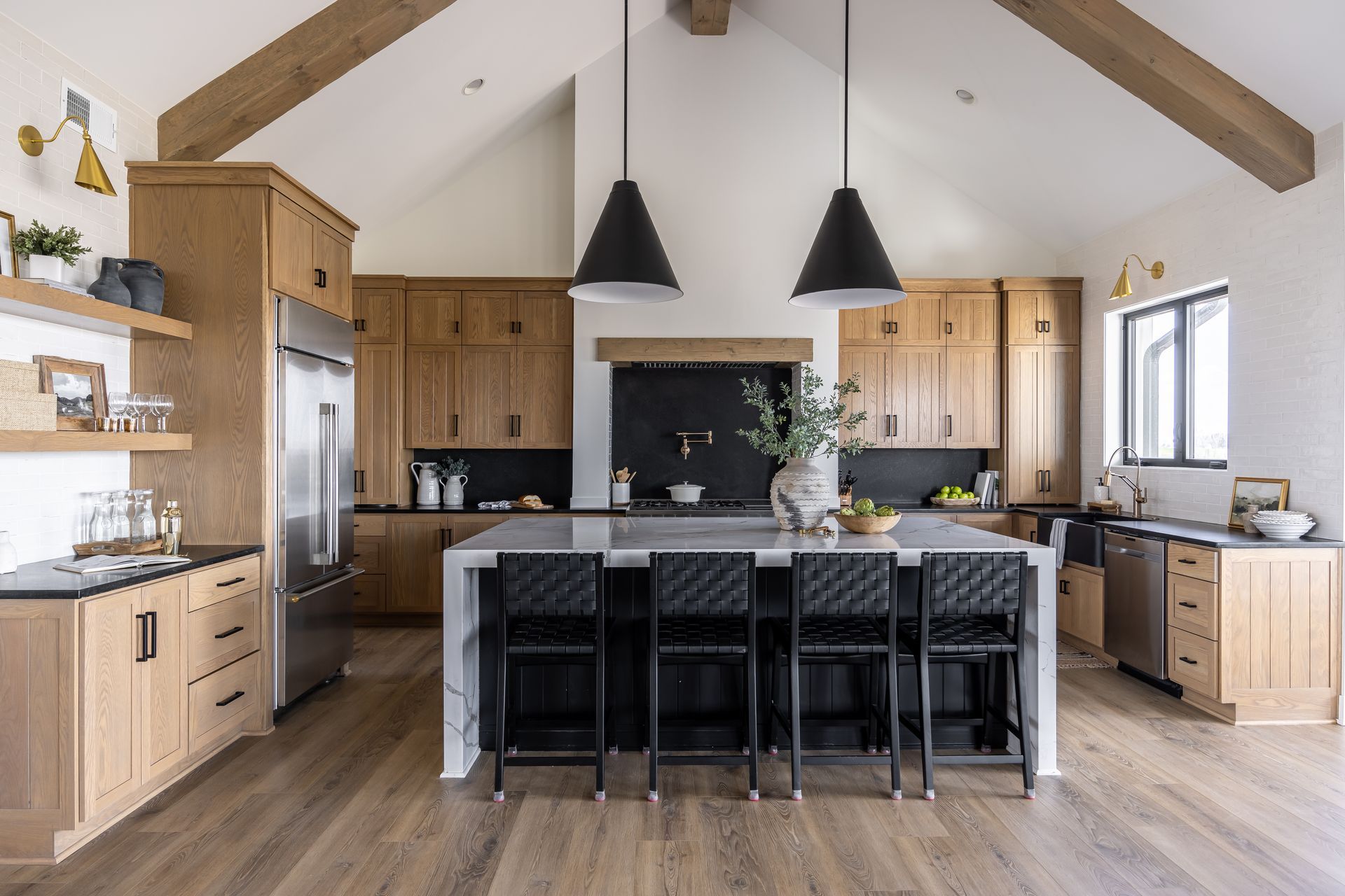 Modern kitchen with wood cabinets, island with stools, and black pendant lights.