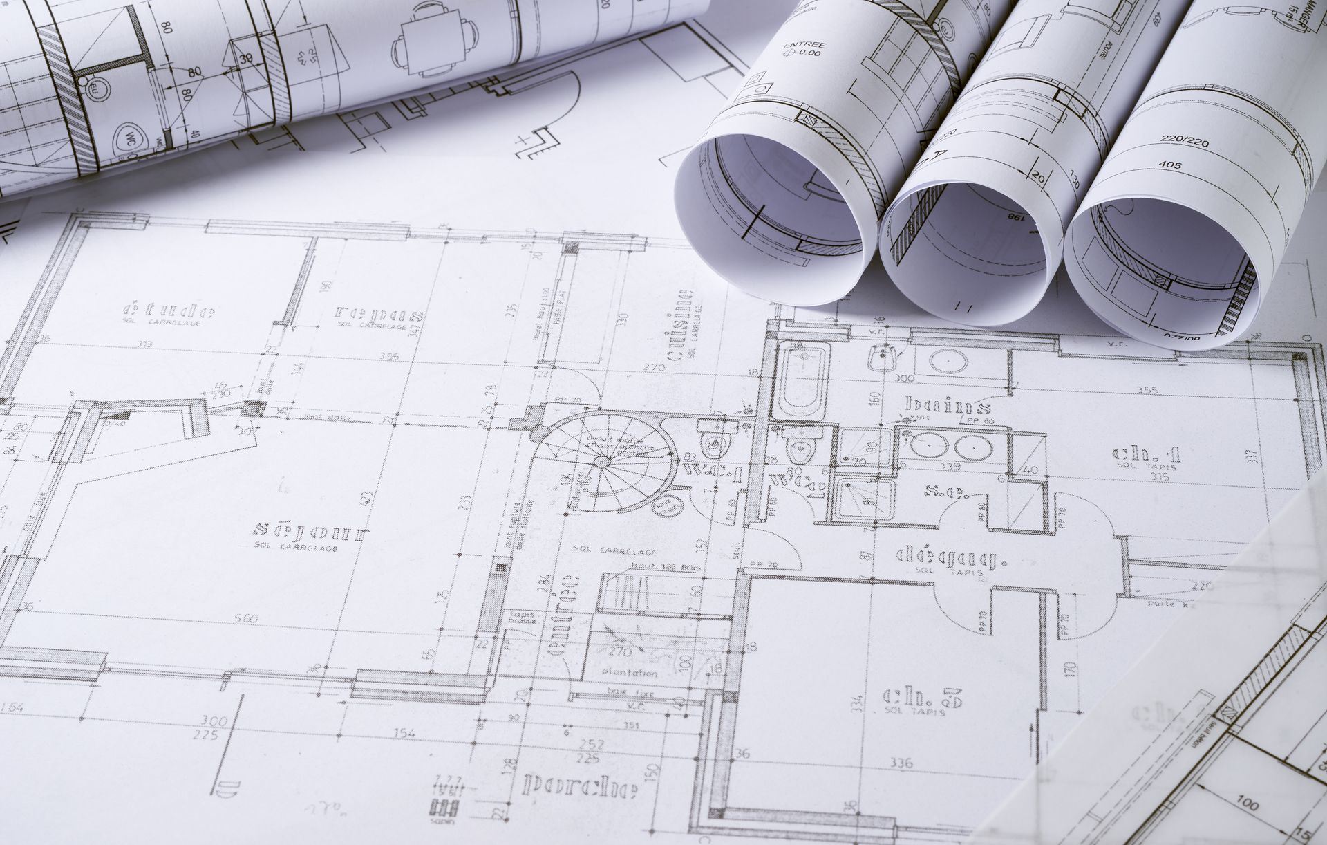 Architectural blueprints, rolled and spread out on a white surface, detailing a building's floor plan.