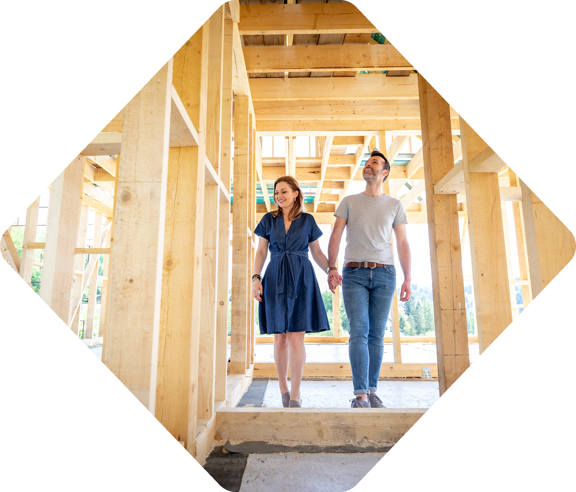 Couple se tenant la main, souriant, marchant à travers la charpente en bois d'une maison en construction.