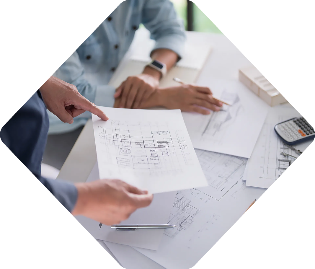 Deux personnes examinant des plans architecturaux, pointant du doigt et discutant des plans.