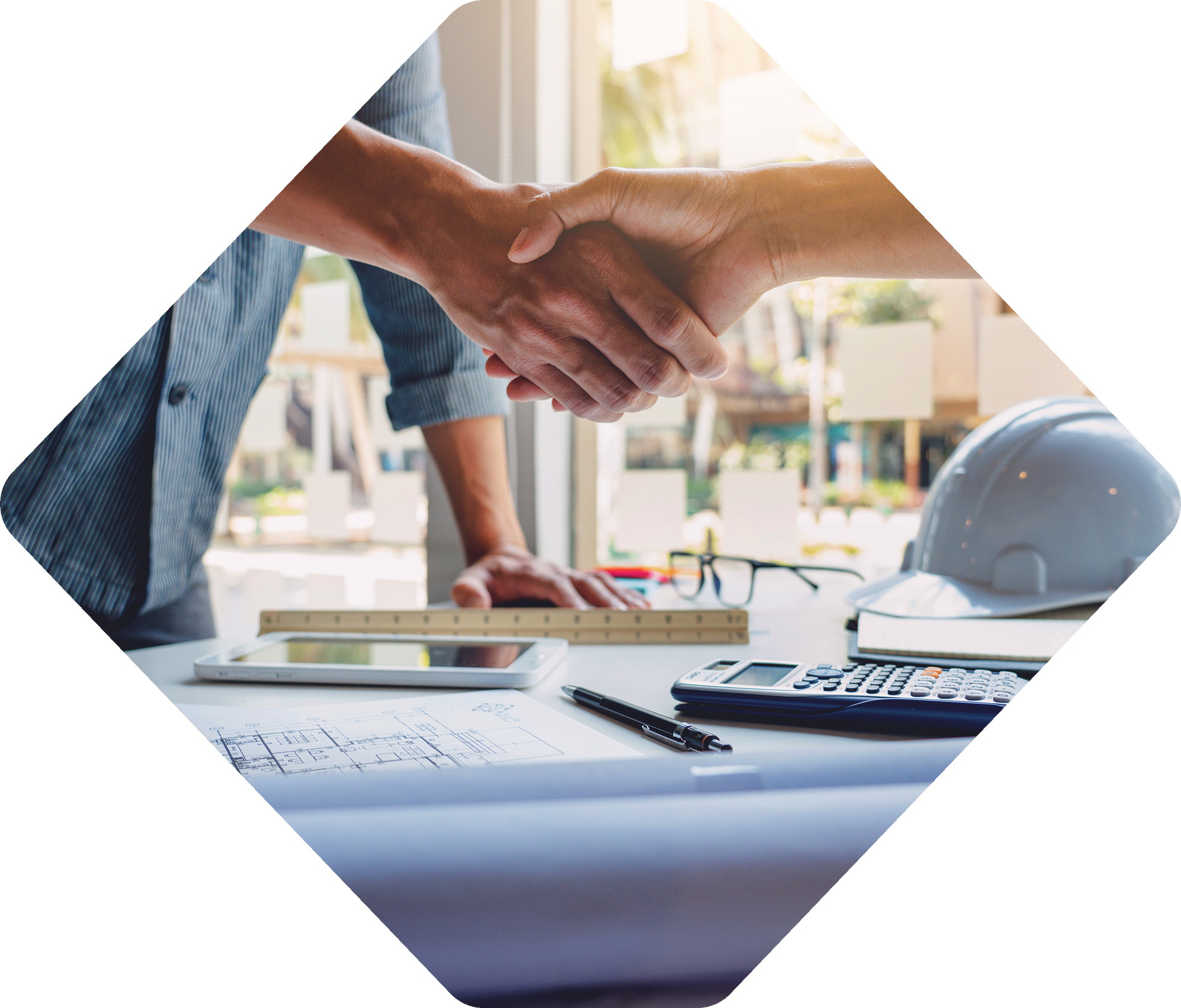 Two people shaking hands over a table with blueprints, tools, and a hard hat; business deal.