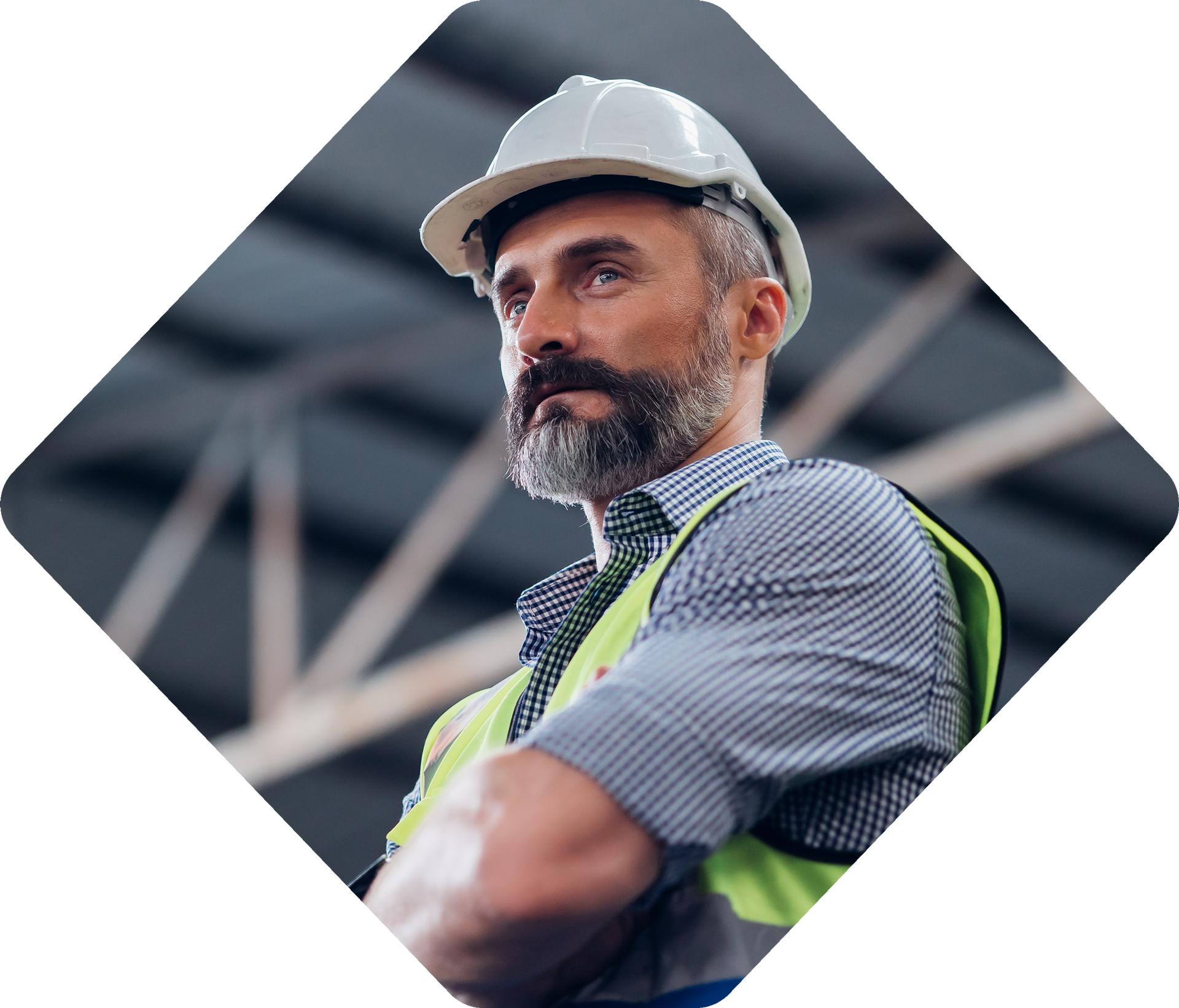 Homme avec une barbe portant un casque et un gilet de sécurité, les bras croisés, l'air pensif dans un entrepôt.