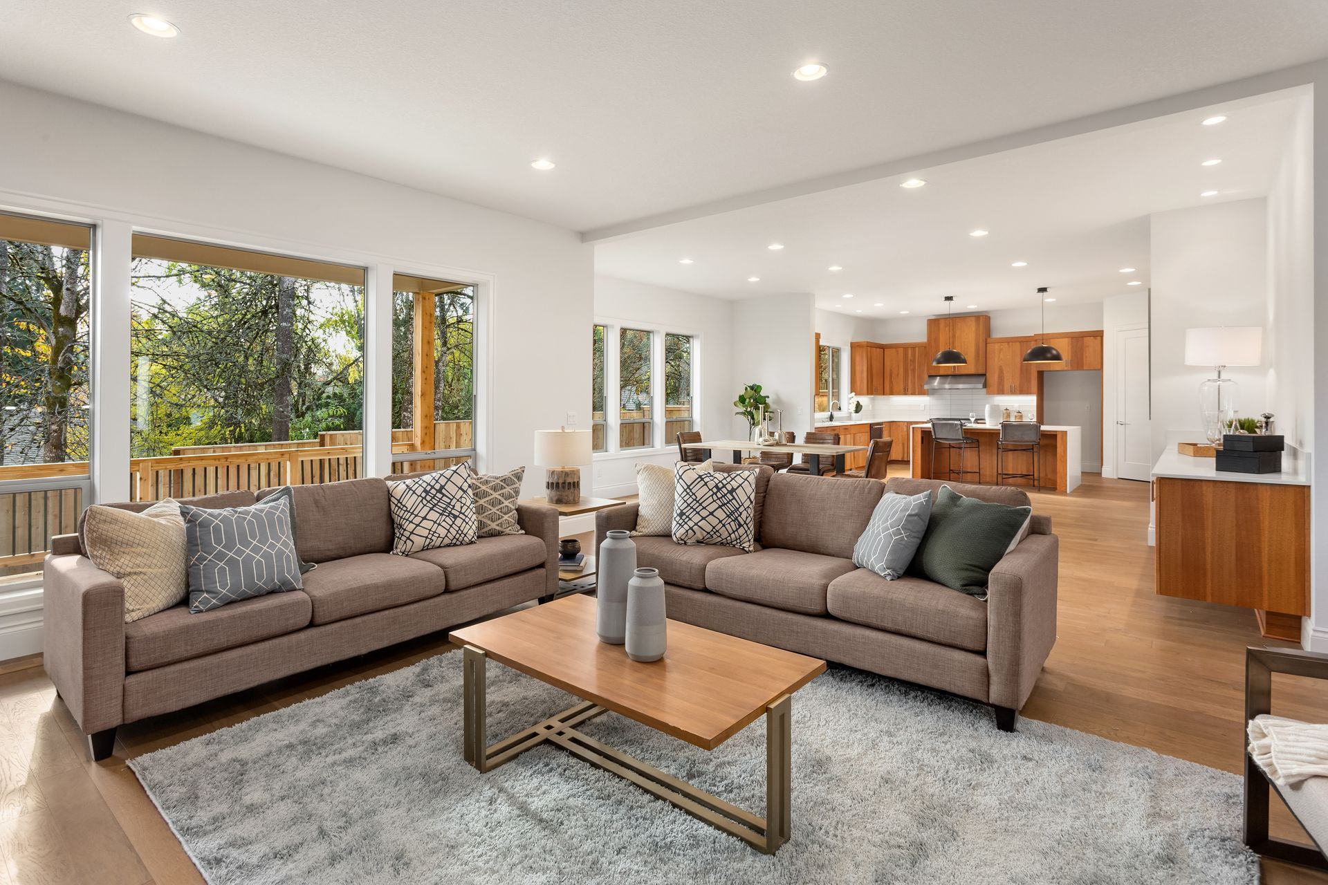 Salon spacieux avec deux canapés marron, une table basse en bois et de grandes fenêtres donnant sur une terrasse.