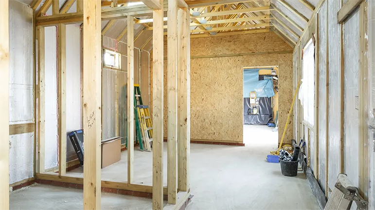 Interior view of a wooden frame construction site. Walls and roof are exposed, showing studs and unfinished surfaces.