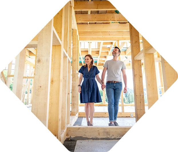 Couple se tenant la main, souriant, marchant à travers la charpente en bois d'une maison en construction.