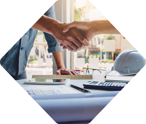Deux personnes se serrant la main autour d'une table avec des plans et des outils de construction.