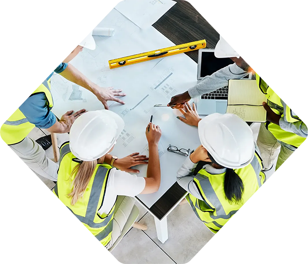 Des ouvriers du bâtiment portant des casques et des gilets de sécurité collaborent sur des plans à une table.