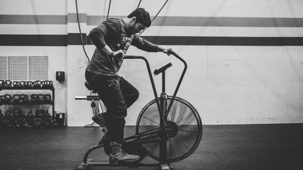 a man wearing a shirt that says crossfit is riding an exercise bike