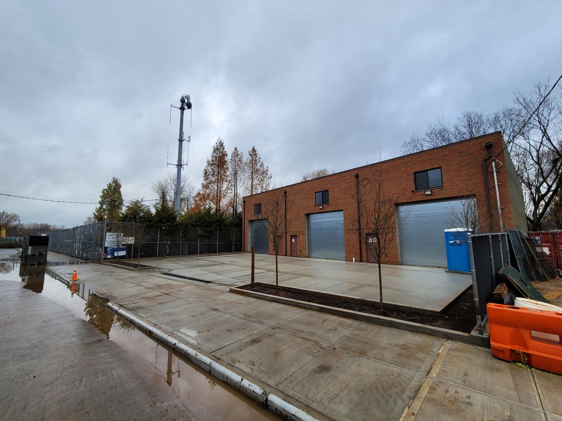 Brick commercial building with three garage doors; cloudy day. Paved lot with puddles.