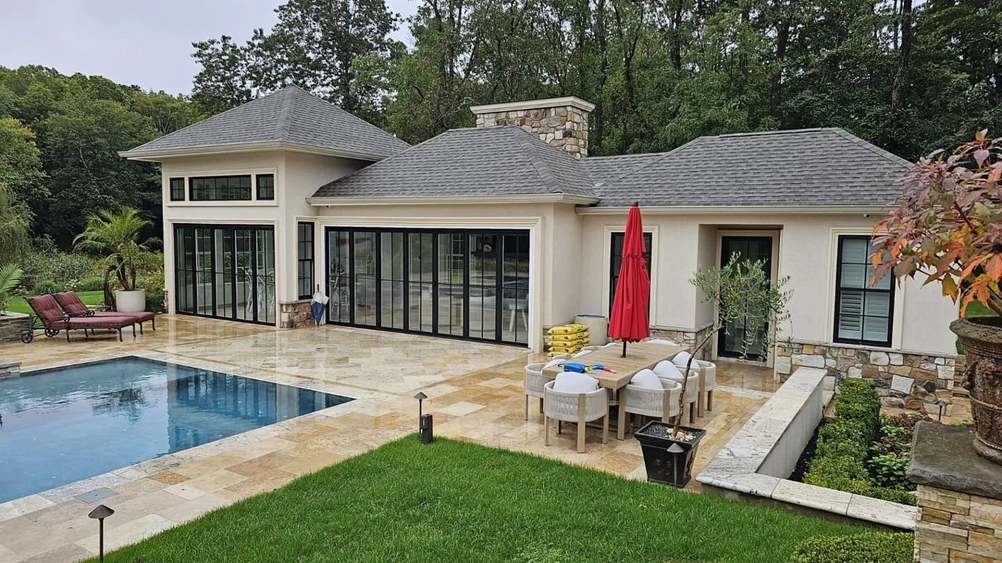 Luxury home with pool, patio, and green lawn. Features a stone chimney and folding glass doors.