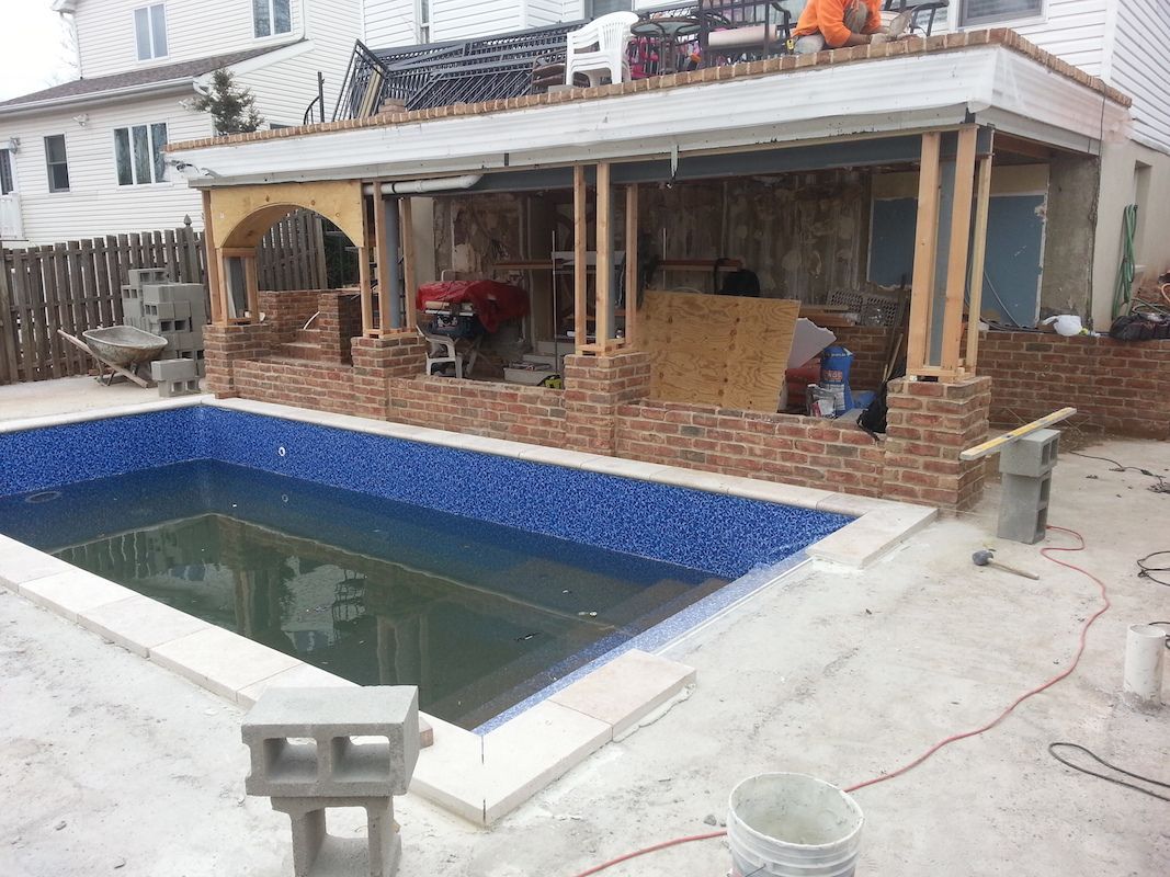 Pool under construction with brick wall, workers, and a covered patio.