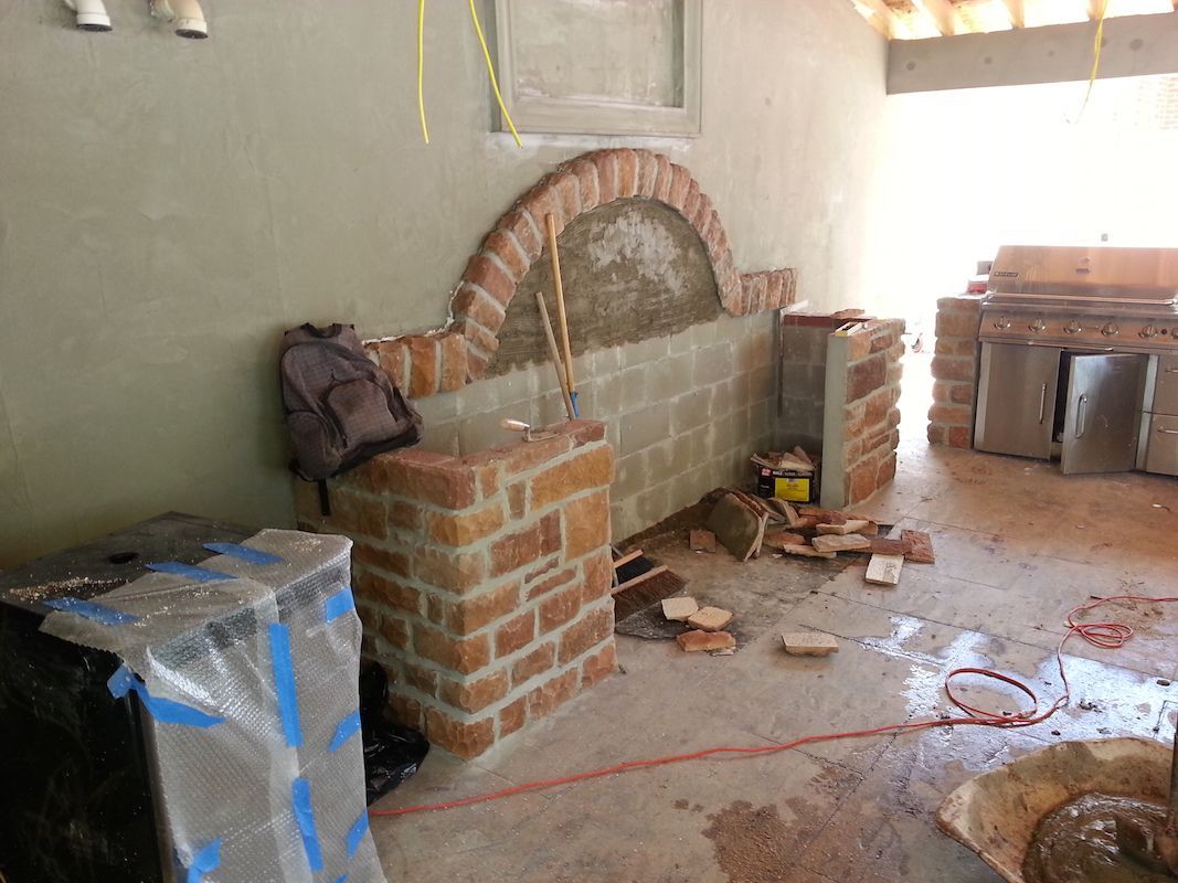Construction of brick outdoor kitchen, with arched brickwork and stone.