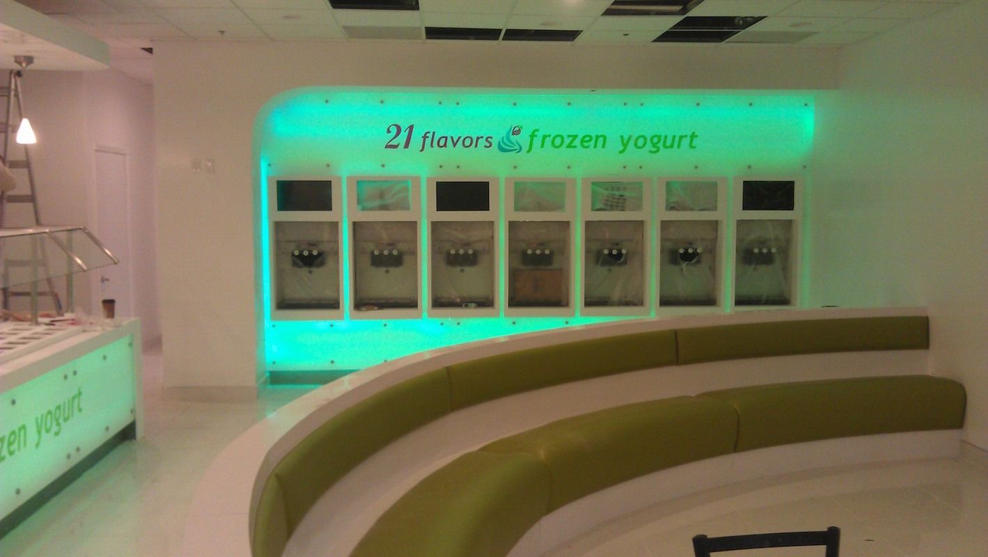 Frozen yogurt shop interior with neon green accents; yogurt machines, curved bench.