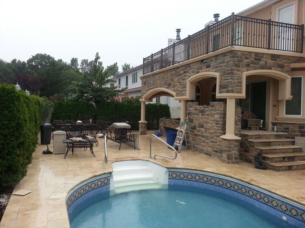Backyard with a swimming pool, stone patio, and two-story house with a balcony.