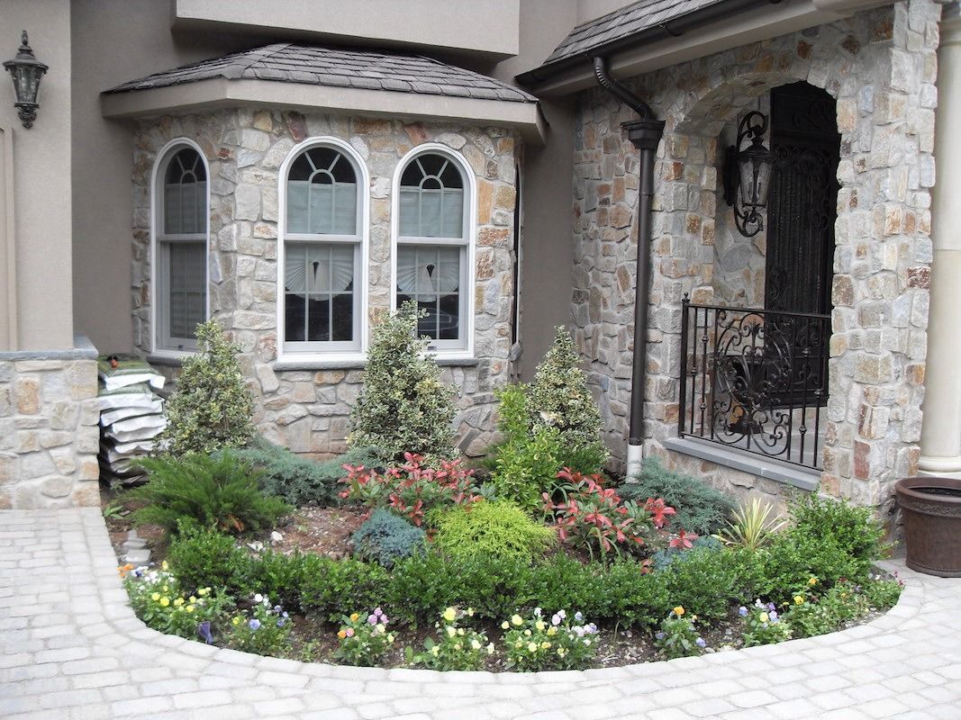 Stone building facade with garden bed of diverse green plants and colorful flowers.