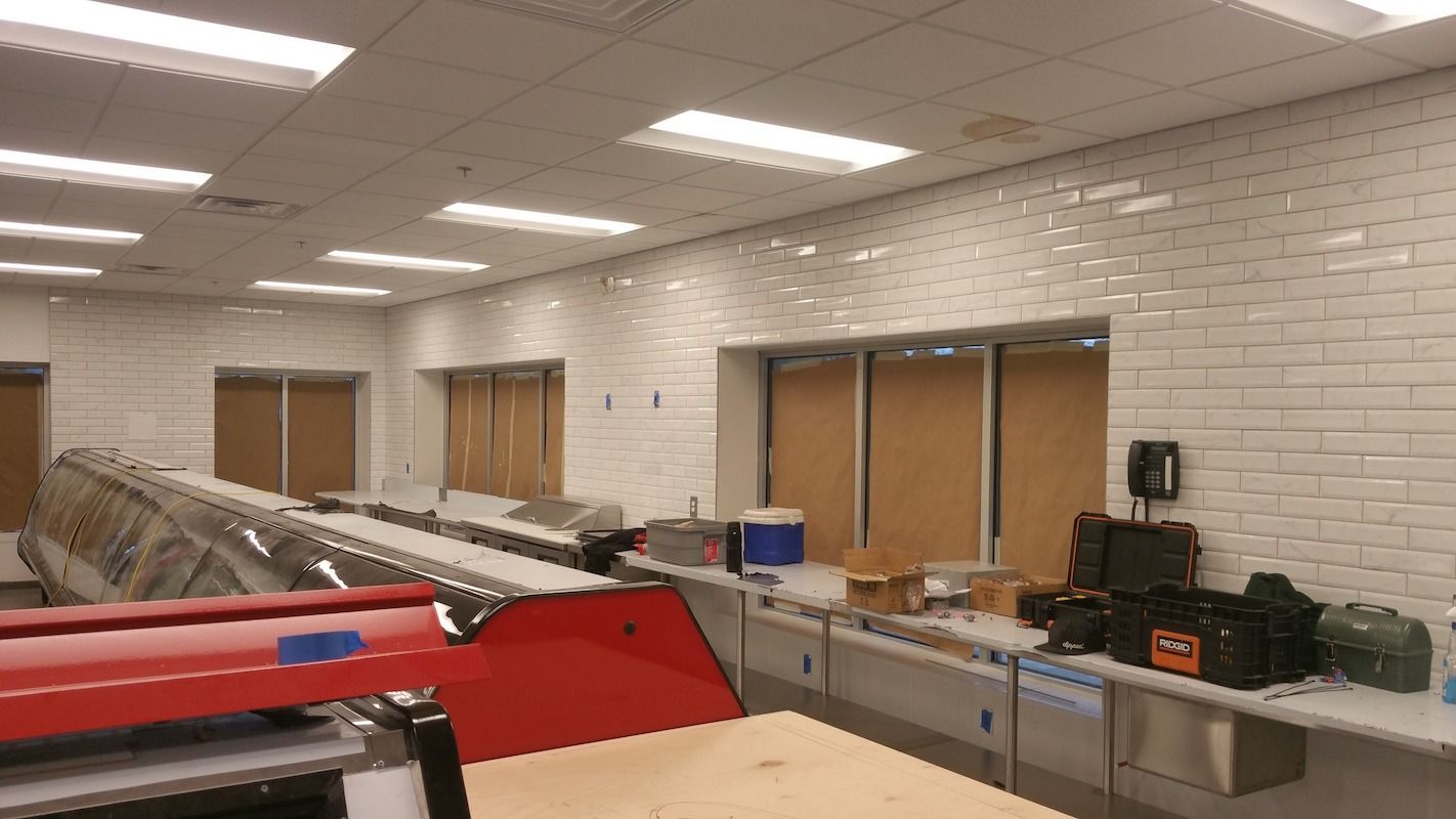 Interior of a commercial kitchen. White tiled walls, equipment, and a service counter.