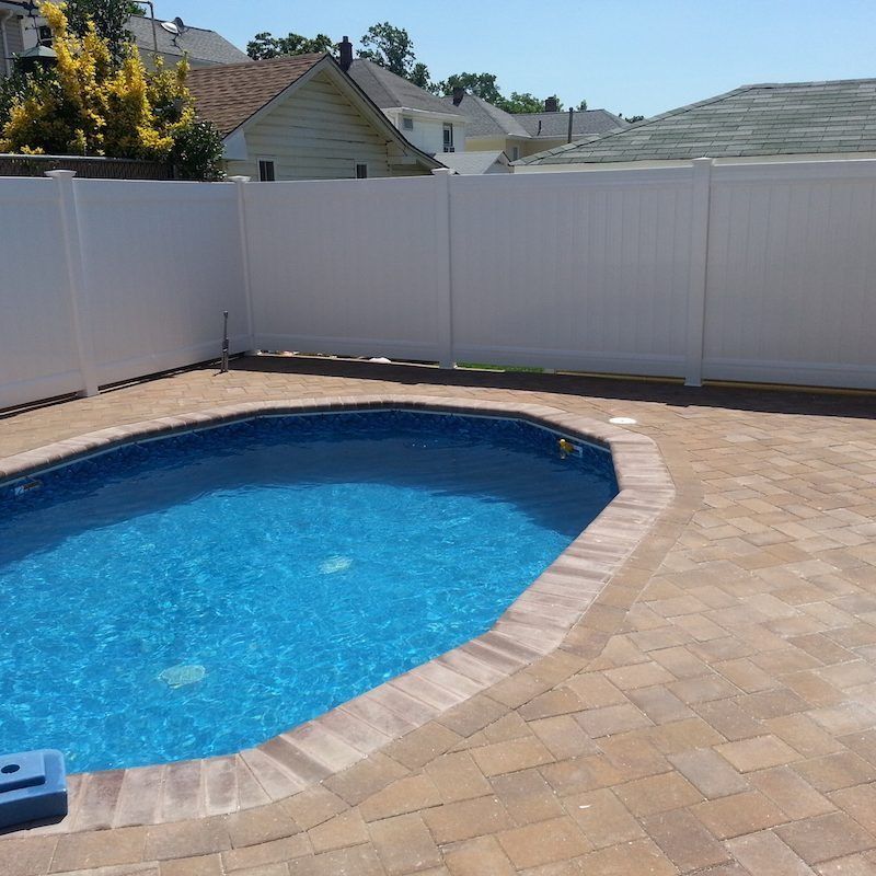 White fenced-in backyard with a blue, octagonal swimming pool and a brick patio.