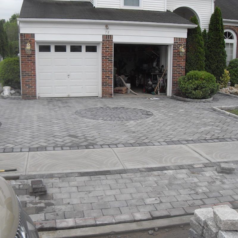 Brick driveway leading to a white garage, gray pavers, and a round design.