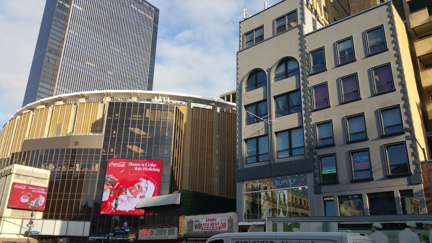 Buildings in a city setting; Madison Square Garden, commercial buildings, and a skyscraper are visible.