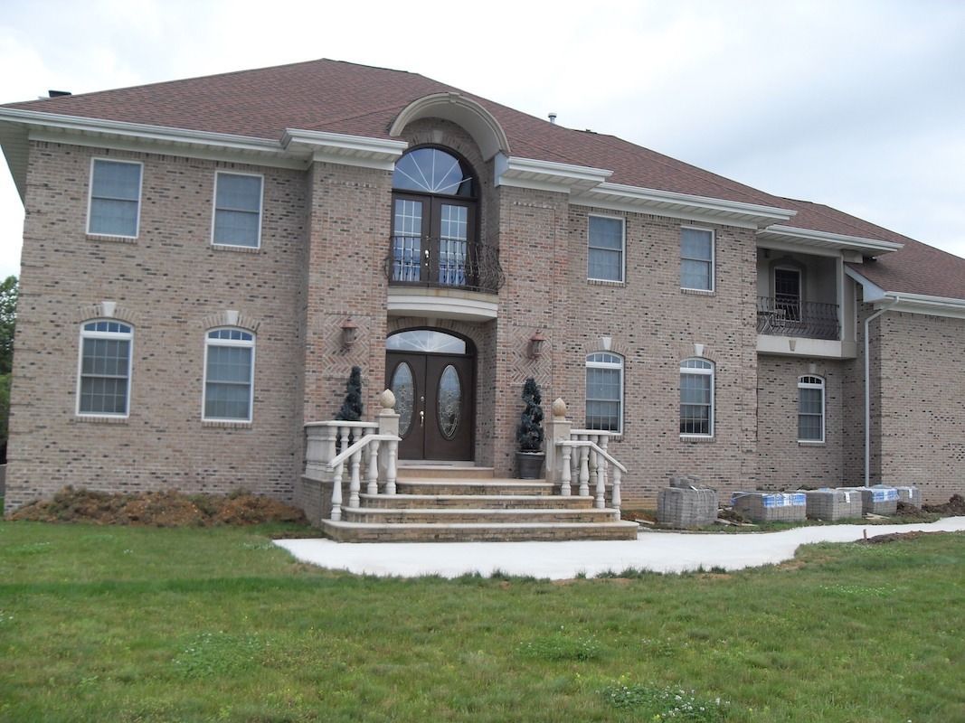 Two-story brick house with brown roof and entryway with steps, in a grassy setting.