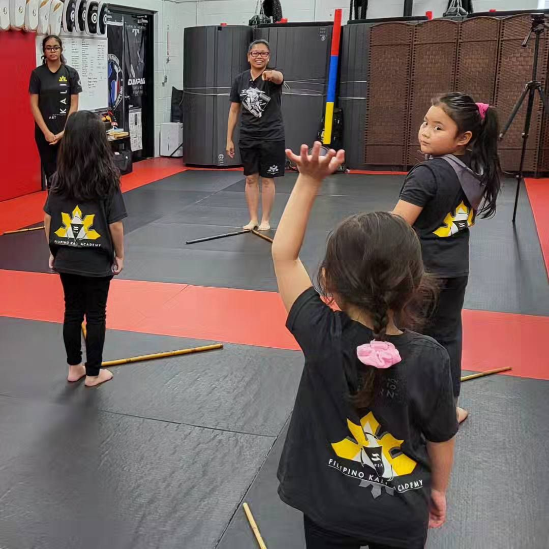 A group of children are practicing karate with a teacher in a gym.