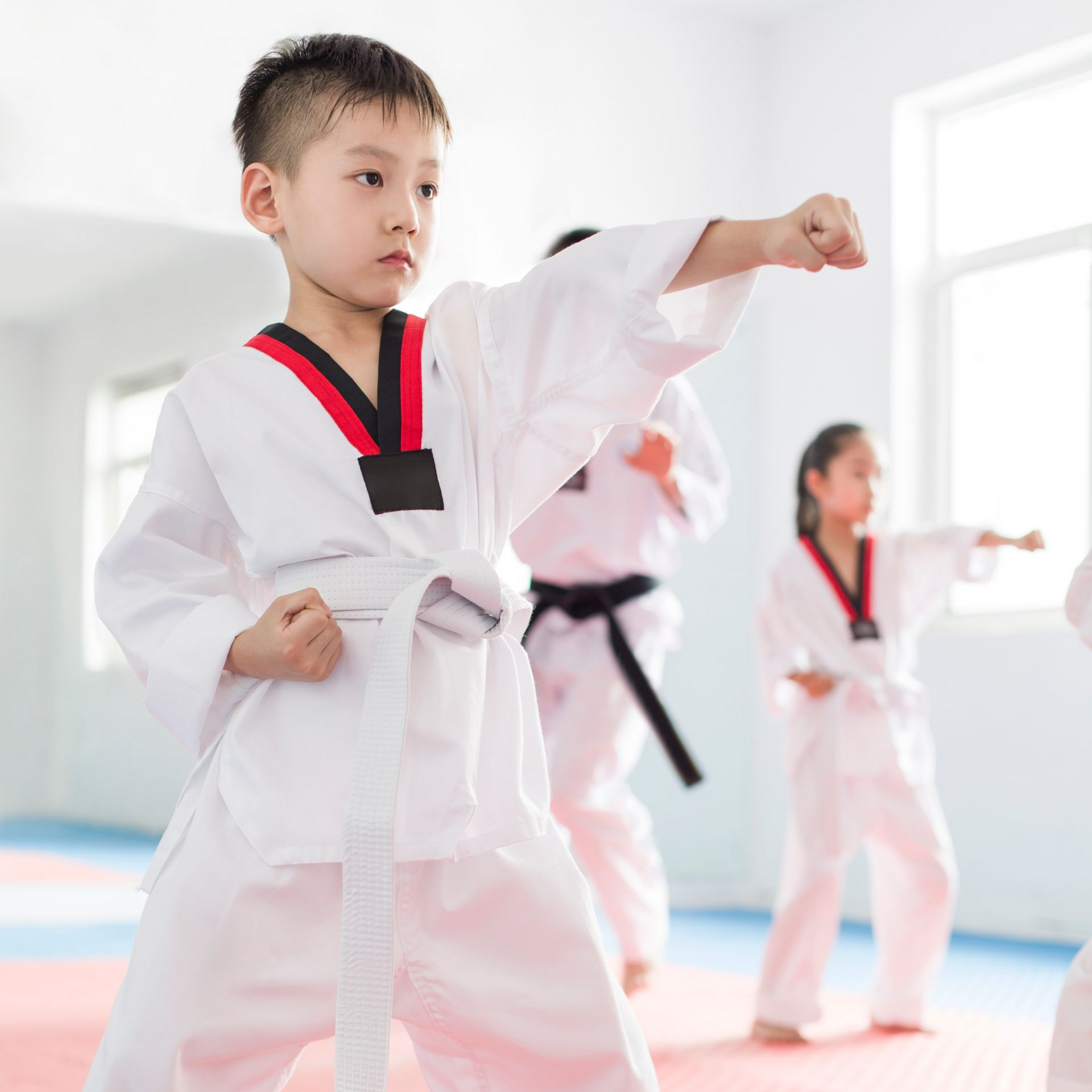 A man is kneeling down next to a young boy in a taekwondo class.