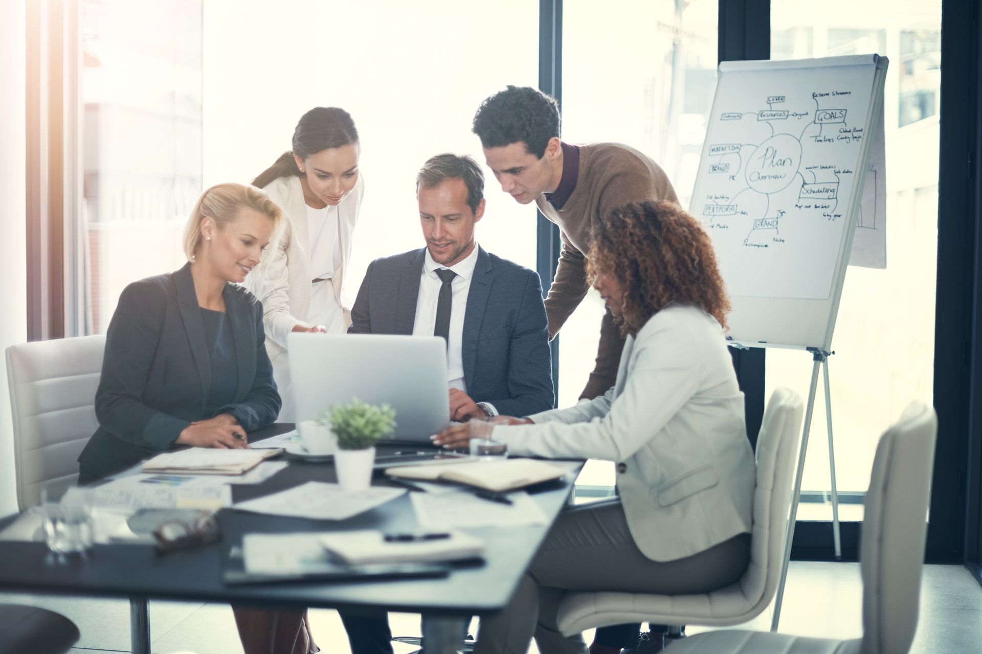 Business team collaborating around a laptop in a bright office meeting room.