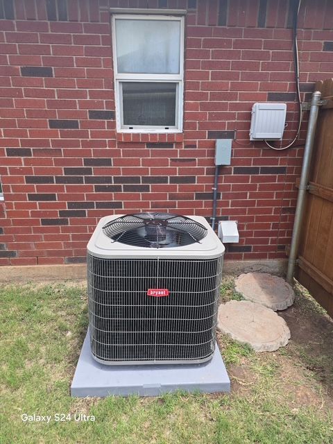 Air conditioning unit against a brick wall, near a window, with electrical components and stone pavers.