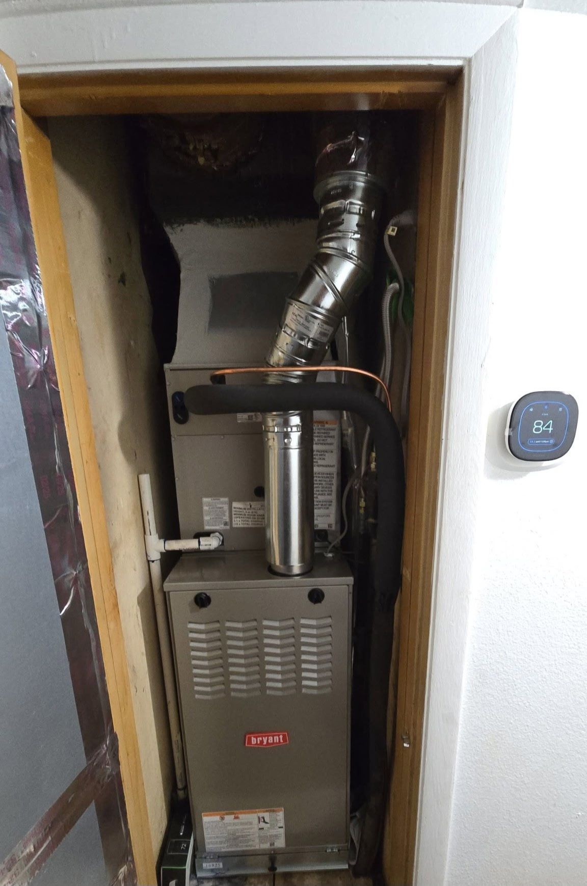 Furnace unit installed in a closet, with vent pipes and thermostat visible.