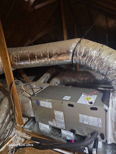 HVAC unit in an attic with insulated ductwork. Brown rafters, silver ducting, and gray unit.