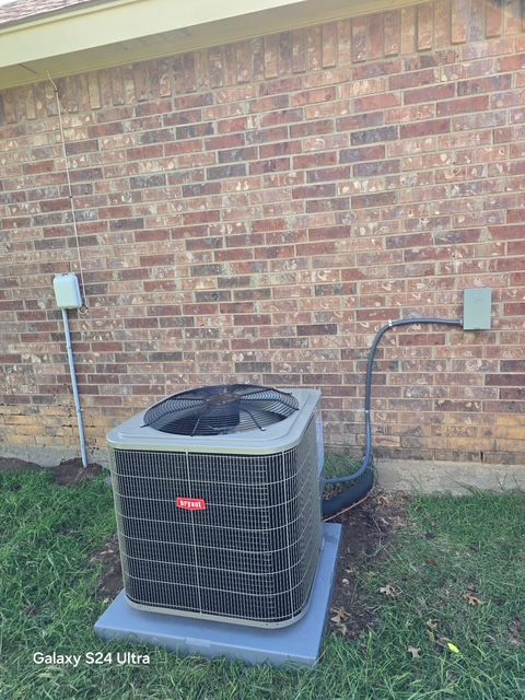 Outdoor air conditioning unit against a brick wall. Electrical boxes and conduit visible.