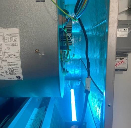 Inside of an air handler, a blue UV light is installed. Wires are visible.
