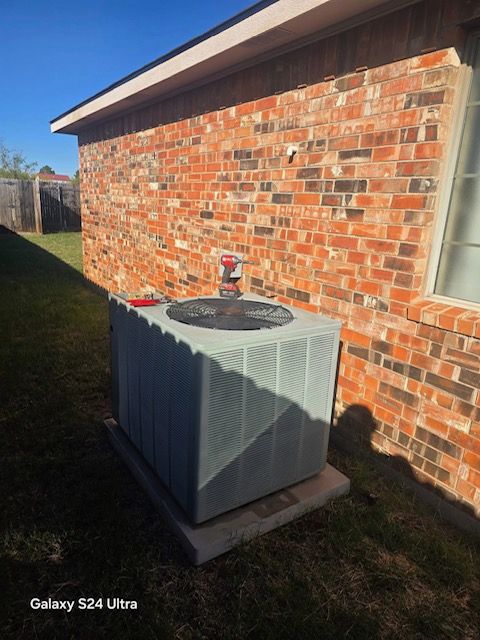 Gray air conditioning unit outside a brick building on a concrete pad, on a sunny day.