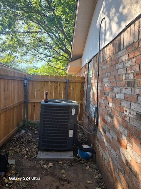 Air conditioning unit next to a brick wall and wooden fence, outdoors.