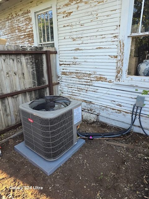 Air conditioning unit next to a weathered white house, beside a fence.